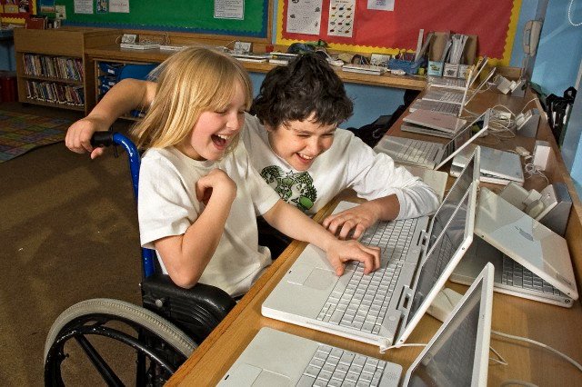 Disabled boy in wheelchair with friend using laptop computer